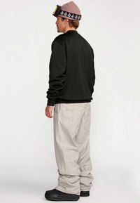 Sweat-shirt noir, pantalon cargo gris clair, chaussures noires. Le mannequin porte un bonnet rose et des lunettes de ski, affichant un style décontracté et superposé.