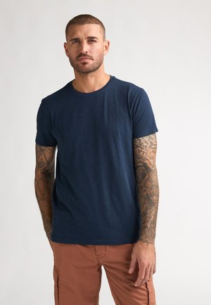 Navy blue short-sleeve t-shirt made of soft fabric, featuring a round neckline and subtle logo detail on the chest. Worn with khaki pants.
