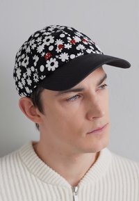 Gorra negra con un patrón de flores blancas y detalles en rojo. Presenta un visera curvada y un diseño ajustado. Textura de tela suave.