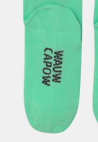 Calzini alla caviglia verde chiaro realizzati in tessuto morbido, con testo nero stampato sulle punte e una texture semplice e liscia.