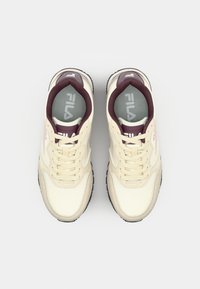 Cream-colored FILA sneakers with maroon accents, featuring a lace-up design, textured overlays, and rubber soles.