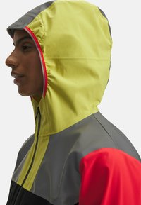 Hoodie in Gelb, Grau und Rot; verfügt über einen Reißverschluss, eine glatte Textur und kontrastierende Farbpaneele. Seitenansicht.