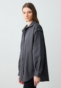 Chemise en charbon gris à boutons avec col, manches longues et coupe décontractée. Texture lisse et détails d'ourlet arrondi.