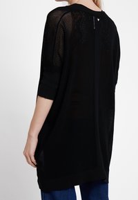 Svart, löst sittande stickad topp med trekvartslånga ärmar, texturerat mönster och rundad halsringning. Har en liten detalj på baksidan.