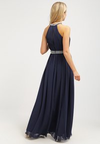 Marinblå maxiklänning med plisserad axelrem och halterneck. Har ett fint smyckat midjeband och flytande tyg som skapar en mjuk silhuett.