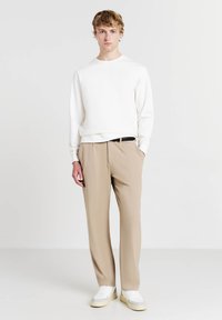 Maglione leggero bianco, pantaloni beige su misura e sneakers bianche. Design semplice con una vestibilità comoda. Texture lisce e colori neutri.