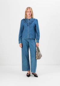 Denim outfit features a ruffled collar blouse and wide-leg pants in light blue. Accessories include a patterned snake-print bag and black shoes.