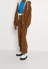 Oranssi ja ruskea leopardi-kuvioinen corduroytakki ja -housut, yhdistettynä siniseen slim-fit paitaaan ja valkoisiin platform-kengiin. Valkoinen vyö korostaa asua.