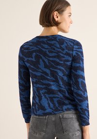 Blaues und dunkelblaues Pullover mit langen Ärmeln, featuring ein welliges Tierdruckmuster und einem runden Halsausschnitt.