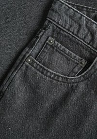 Jeans de mezclilla negra con un bolsillo frontal con acentos de botón, costuras visibles y una tela texturizada con un ligero brillo.