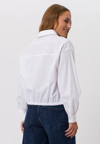 Witte cropped blouse met lange, pofmouwen en een elastische zoom. De achterkant heeft een subtiele naaddetail. Gecombineerd met donkerblauwe denim.