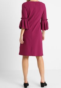 Fuchsia klänning med utsvängda, volangärmar, dragkedja bak, och en jämn textur, med en kjol som når knäna.