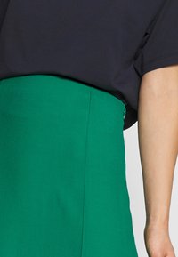 Zwarte oversized top met een ronde halslijn boven een groene, gestructureerde hoge taille rok met een zijsluiting. Zachte stof contrasteert kleuren.