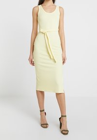 Gul ribbad midiklänning med rundad halsringning, midja med bälte och rak silhuett. Matchad med gröna klacksandaler.
