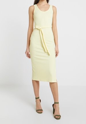 Abito midi giallo a coste con scollatura a barchetta, vita con cintura e silhouette dritta. Abbinato a sandali con tacco verde.