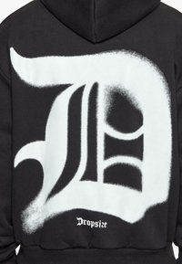 Schwarzer Kapuzenpulli mit einem großen, weißen, graffiti-artigen Buchstaben D auf dem Rücken, darunter in kleiner Schrift der Text "Dropsize".