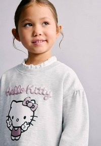 Hanorac gri cu un grafic Hello Kitty în negru și roz, cu un guler alb cu volane și textură moale, într-o croială lejeră.