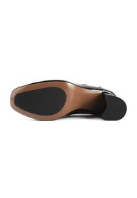 Semelle de chaussure en cuir noir avec une semelle intermédiaire lisse de couleur brun clair, un talon en caoutchouc noir texturé et une forme incurvée et allongée.