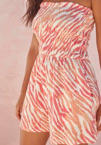Mono sin tirantes en una tela ligera y texturizada con un patrón de rayas tigre en rosa y blanco. Presenta una cintura fruncida y un corte holgado.
