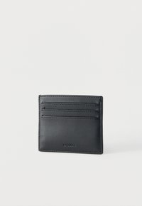 Μαύρο δερμάτινο θήκη καρτών με τρεις οριζόντιες θήκες για κάρτες και ανάγλυφο λογότυπο Lacoste στο κάτω κέντρο σε λευκό φόντο.