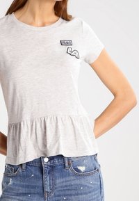 Top gris de manga corta con un dobladillo peplum, que cuenta con parches bordados de "PARADISE LA". Hecho de un tejido suave con un ajuste casual.