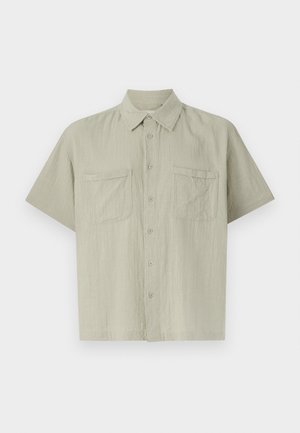 Svijetlo siva, kratkoslijeva košulja od teksturirane tkanine. Ima gumbe sprijeda i dva džepa na prsima. Klasičan dizajn kragne.