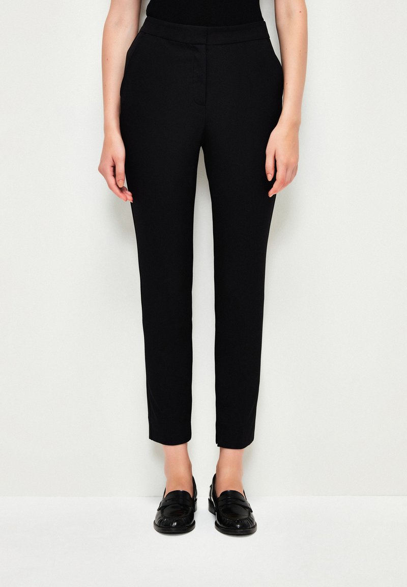 Svarta skräddarsydda byxor med slim fit, tillverkade av ett slätt tyg, med avsmalnande ben och midjehögt resår. Bärs med svarta loafers.