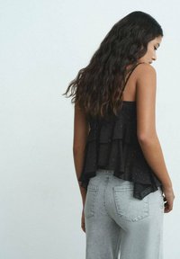 Svart genomskinlig topp med lager och prickigt mönster, åtsittande remmar, lager av volanger, i kombination med högmidjade ljusgrå jeans.