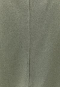 Primo piano di tessuto lavorato a maglia verde oliva con una cucitura verticale centrale e dettagli di cucitura visibili.