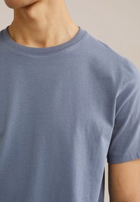 Světle modré tričko s kulatým výstřihem vyrobené z měkké bavlny. Má hladkou texturu, krátké rukávy a jednoduchý design. Bez vzorů a akcentů.