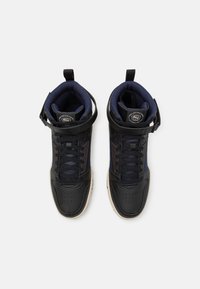 Pár černých a námořnických vysokých tenisek s polstrovanými límci, tkaničkami a popruhy na kotník na bílém pozadí.