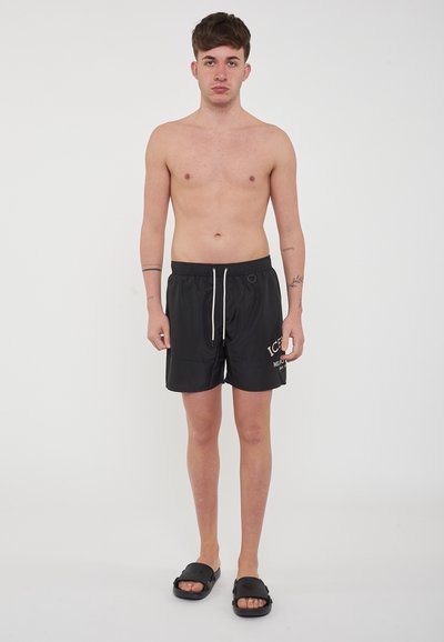 Costumi da bagno neri con vita regolabile e dettaglio del logo. Indossati con sandali neri a ciabatta. Design semplice, realizzati in un tessuto leggero.