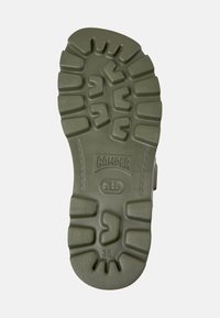 Green rubber shoe sole with deep tread patterns, featuring the word "CAMPER" and size "38" embossed. Textured for grip and durability.