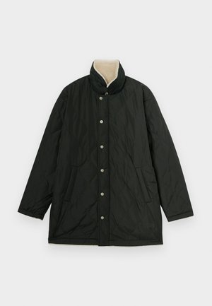 Melnā quiltēta jaka ar augstu apkakli, sudraba pogām, sānu kabatām un bežā odere apkaklē, lai pievienotu tekstūru.