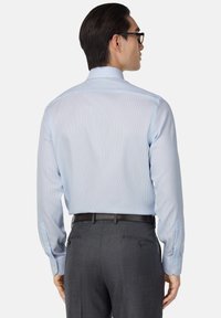 Camicia a righe blu chiaro con colletto standard, maniche lunghe e polsini con bottoni, indossata con pantaloni grigi scuri su misura.