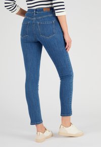 Jean skinny en denim, à taille haute, avec des poches arrière et des détails de couture subtils, associés à des baskets blanches avec des accents dorés.