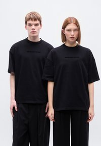 Μαύρα υπερμεγέθη T-shirts με κοντά μανίκια και λαιμόκοψη. Κείμενο "BROKE SINCE MILANO" σε μαύρο χρώμα στο στήθος. Συμπληρωματικό μαύρο παντελόνι.