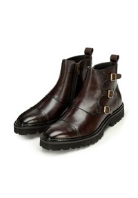 Botas de tobillo de cuero marrón con punteras redondeadas, cremalleras laterales y tres herrajes dorados. Suelas de goma texturizada negra para mayor agarre.