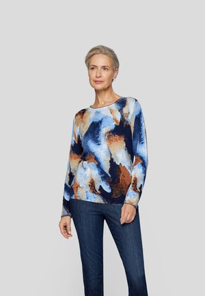 Long-sleeve knit top featuring an abstract blue, brown, and orange pattern, round neckline, and relaxed fit. Paired with dark jeans.