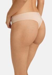 Beige string met een zachte textuur en minimale bedekking. Heeft een laag uitgesneden taille en een naadloos ontwerp, wat een slank silhouet biedt.
