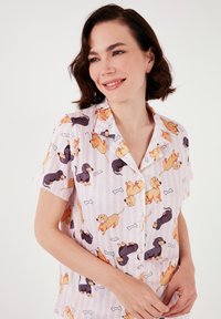 Pajama majica kratkih rukava s rozo prugastim uzorkom koja prikazuje razne crtane pse i kosti. Izrađena od laganog materijala s gumbima sprijeda.