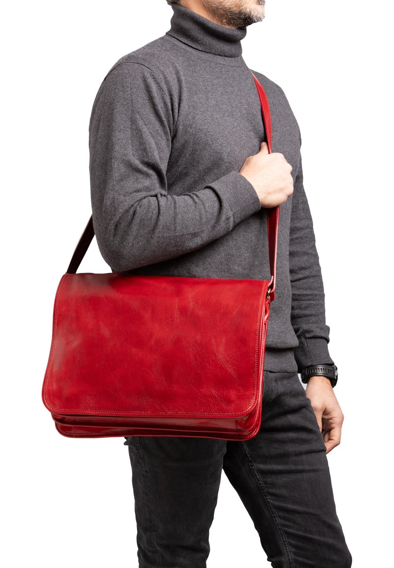 Uomo con dolcevita grigio e orologio nero tiene in mano una grande borsa a tracolla in pelle rossa.