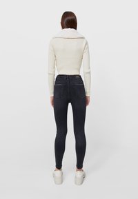 Suéter de crema acanalado con un cuello ancho, combinado con jeans skinny de mezclilla gris oscuro de tiro alto, usados con zapatillas de plataforma blancas.