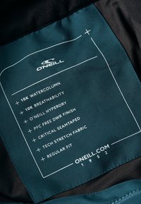 Etikett med O'Neill-logotyp, teal tyg med vit text som beskriver 10k vattensäule, andningsförmåga, DWR-beläggning och kritisk sömtejpning.