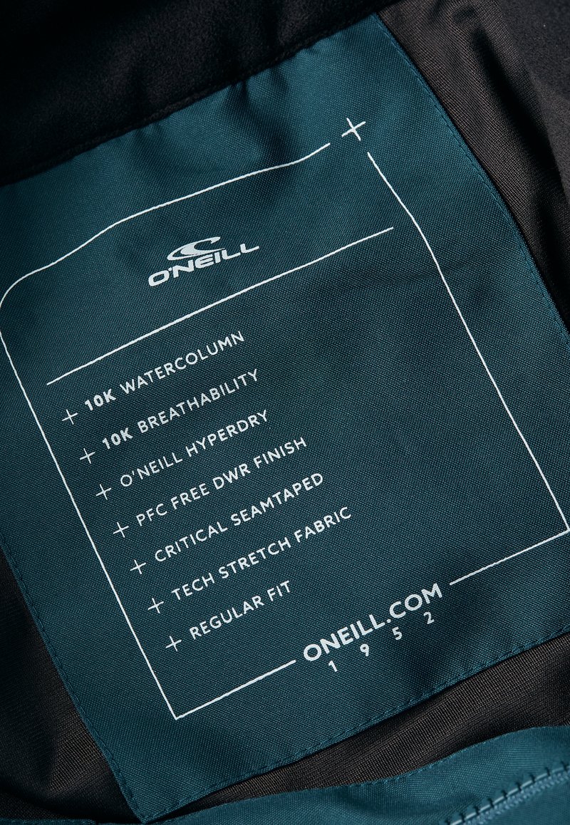 Labeltag met O'Neill-logo, teal stof met witte tekst die details geeft over een waterkolom van 10k, ademend vermogen, DWR-afwerking en kritieke naadvoering.