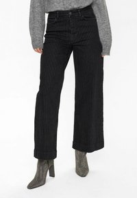 Svartrandiga vida jeans med hög midja, med knappstängning och uppvikta fållar, kombinerat med texturerade metalliska klackboots.