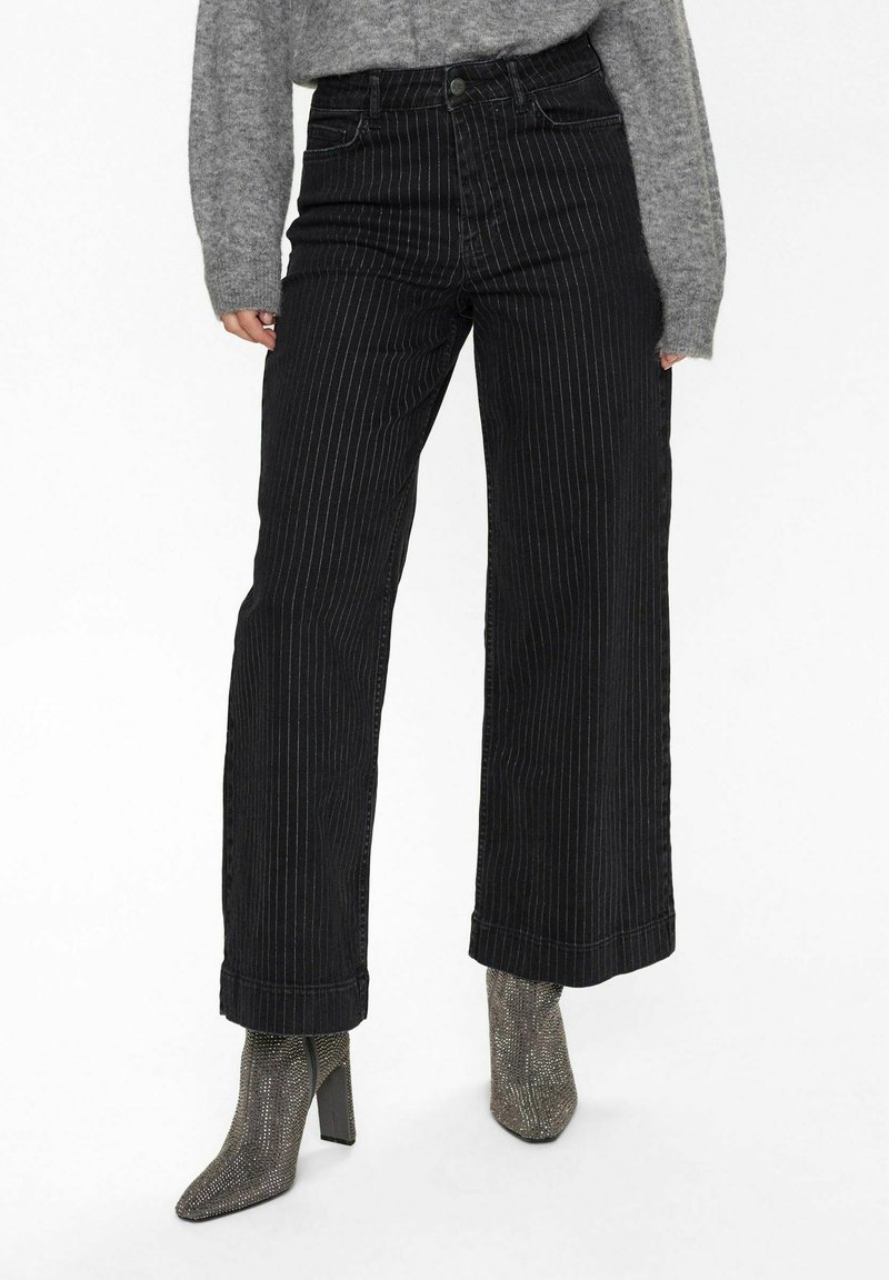 Svartrandiga vida jeans med hög midja, med knappstängning och uppvikta fållar, kombinerat med texturerade metalliska klackboots.