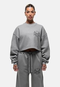 Felpa grigia corta con maniche ampie, con una grafica di una farfalla sul petto, abbinata a pantaloni della tuta grigi con cintura elastica.