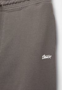 Baumwollsweatpants in einem gedämpften Grauton mit strukturiertem Material, elastischem Taillenbund und kleinem weißen Logo am Unterschenkel.