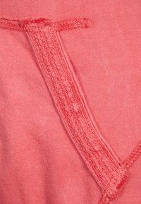 Ribbade korallfärgad sweatshirt-tyg med en texturerad söm och stickningsdetalj. Slät, mjuk textur med en avslappnad passform.